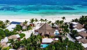 Aerial view of UMusic Hotel & Beach Club Tulum on the Caribbean coast, surrounded by turquoise waters, white sand and tropical greenery.